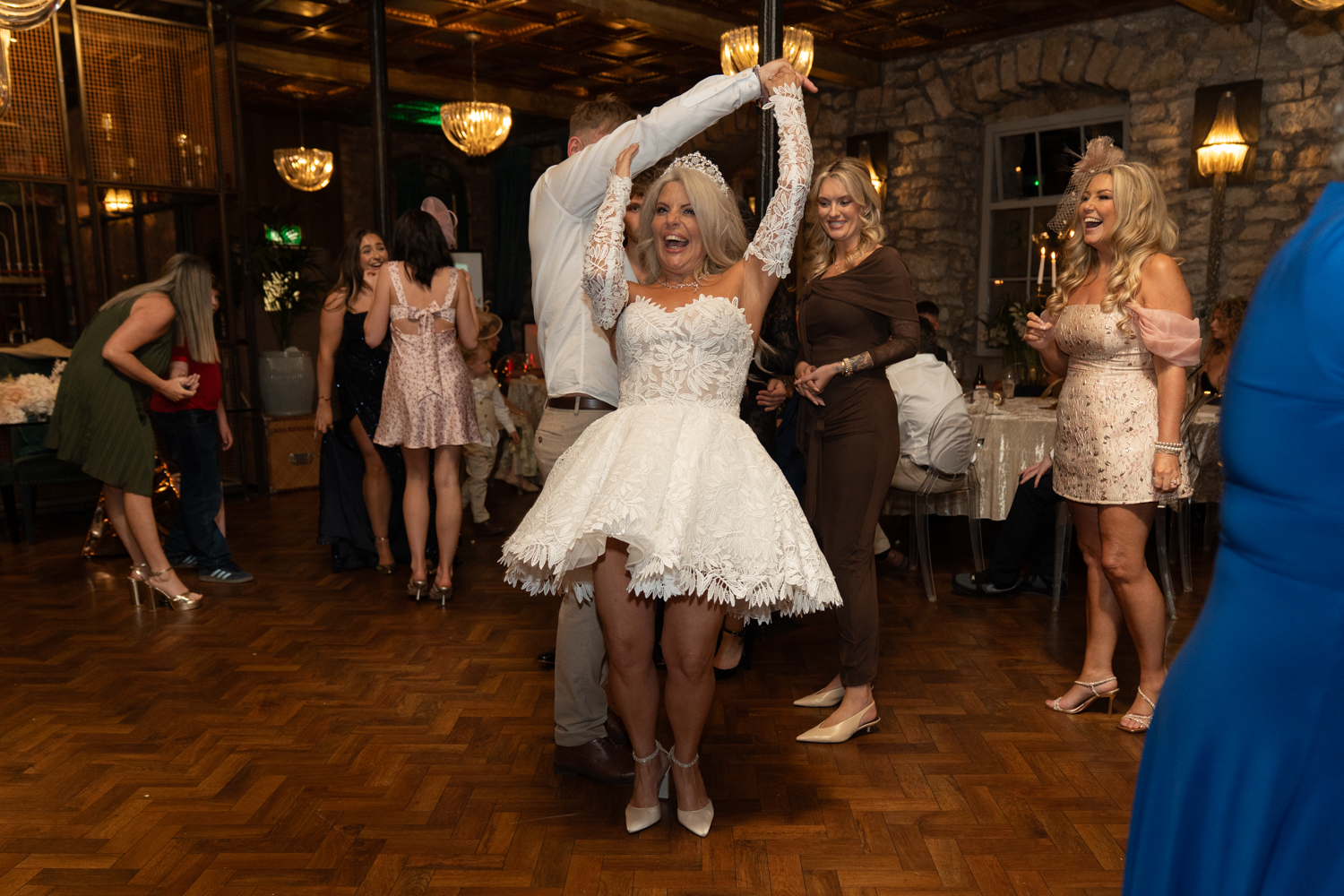 The groom spins the bride — her short dress fanning out, laughter filling the room, guests cheering around them